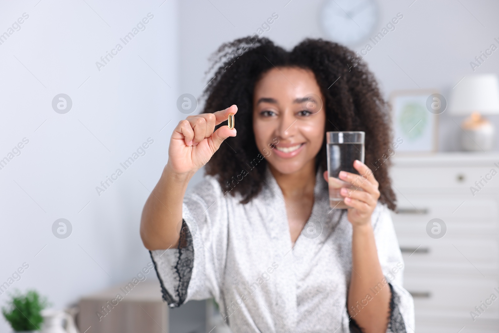 Beautiful Brazilian woman with glass of water and collagen pill indoors, selective focus Photo of Beautiful Brazilian woman with glass of water and collagen pill indoors, selective focus