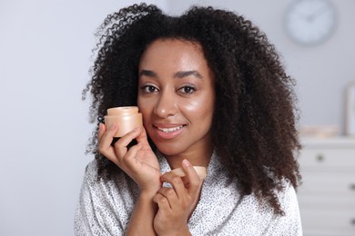 Photo of Beautiful Brazilian woman with jar of collagen cream indoors