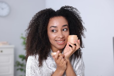 Photo of Beautiful Brazilian woman with jar of collagen cream indoors