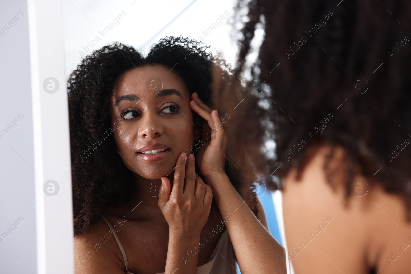 Beautiful Brazilian woman with healthy skin looking at mirror indoors Photo of Beautiful Brazilian woman with healthy skin looking at mirror indoors