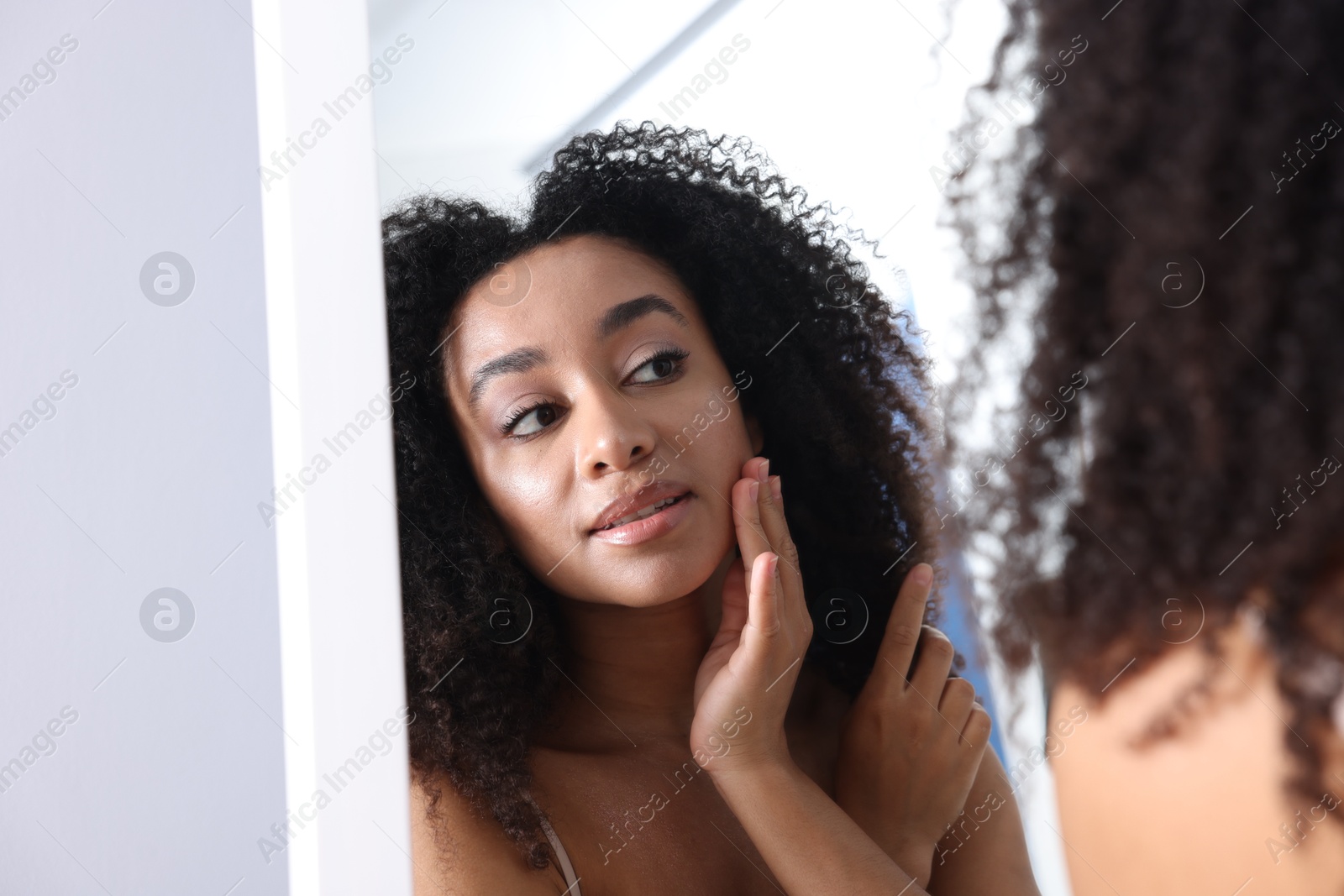 Beautiful Brazilian woman with healthy skin looking at mirror indoors Photo of Beautiful Brazilian woman with healthy skin looking at mirror indoors