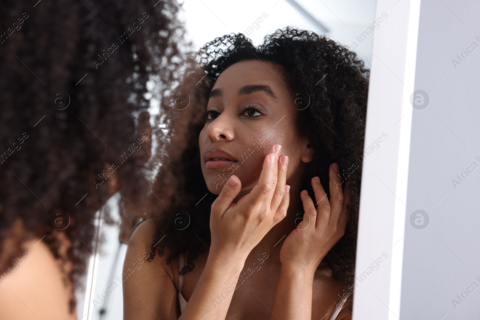 Beautiful Brazilian woman with healthy skin looking at mirror indoors Photo of Beautiful Brazilian woman with healthy skin looking at mirror indoors
