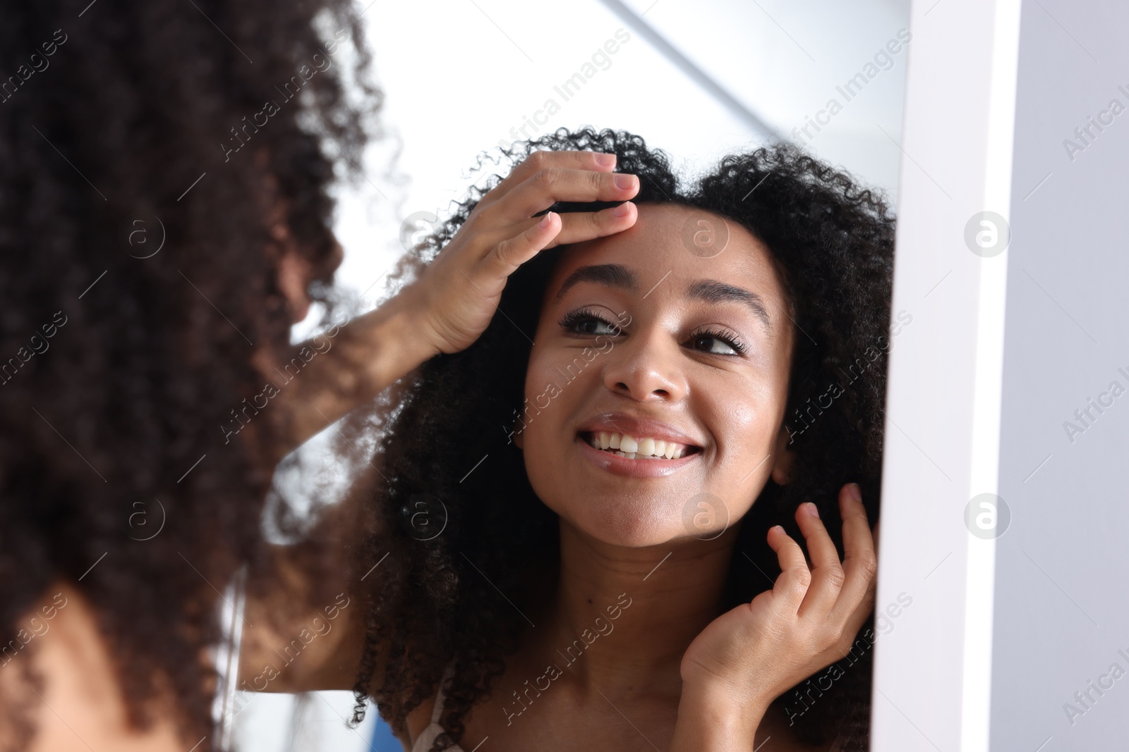 Beautiful Brazilian woman with healthy skin looking at mirror indoors Photo of Beautiful Brazilian woman with healthy skin looking at mirror indoors