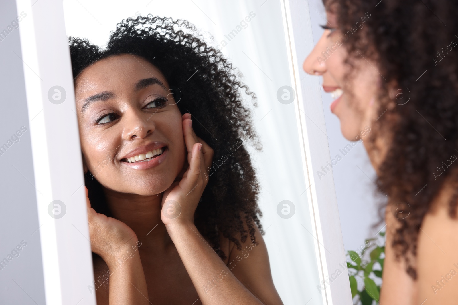 Beautiful Brazilian woman with healthy skin looking at mirror indoors Photo of Beautiful Brazilian woman with healthy skin looking at mirror indoors