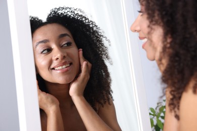 Photo of Beautiful Brazilian woman with healthy skin looking at mirror indoors