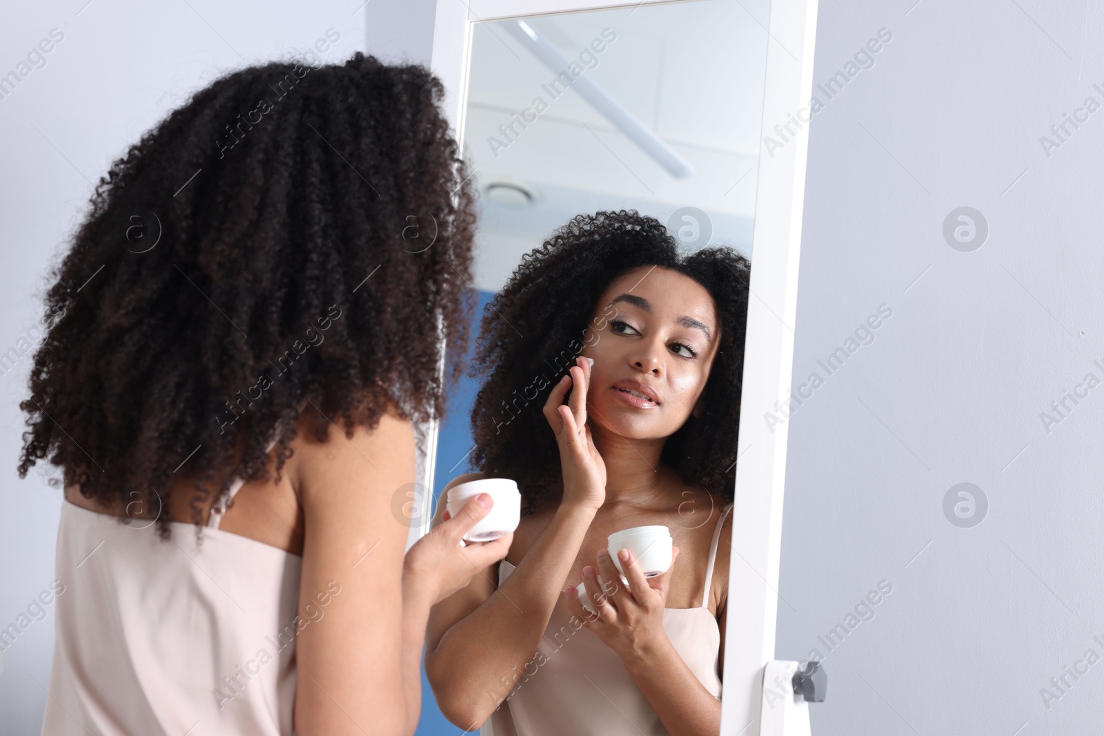Beautiful Brazilian woman with healthy skin looking at mirror indoors Photo of Beautiful Brazilian woman with healthy skin looking at mirror indoors
