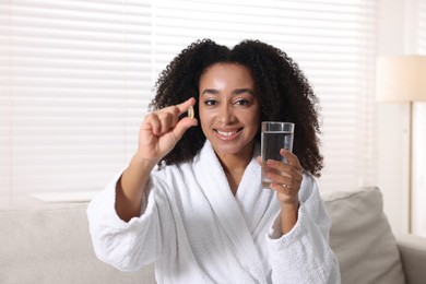 Photo of Beautiful Brazilian woman with glass of water and collagen pill indoors