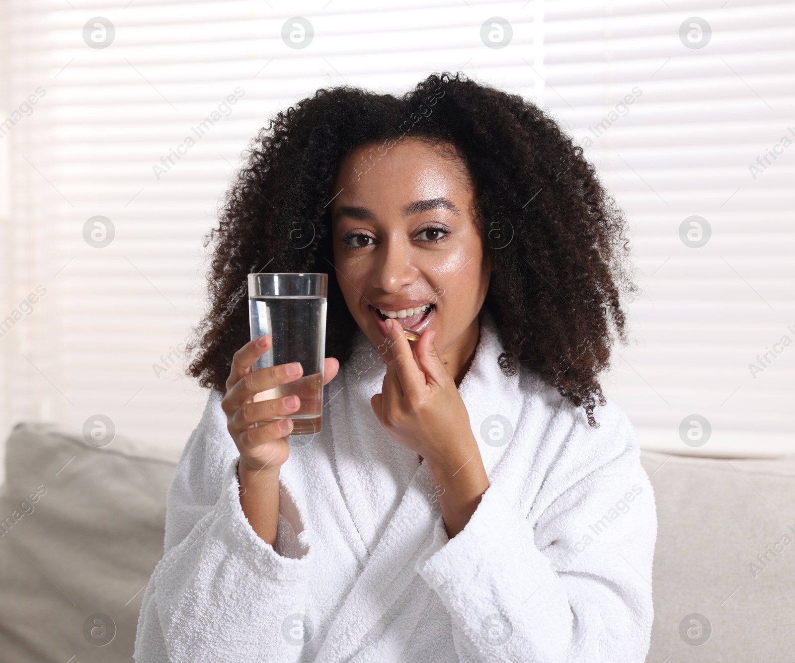 Beautiful Brazilian woman with glass of water and collagen pill indoors Photo of Beautiful Brazilian woman with glass of water and collagen pill indoors