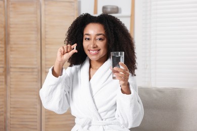 Photo of Beautiful Brazilian woman with glass of water and collagen pill indoors