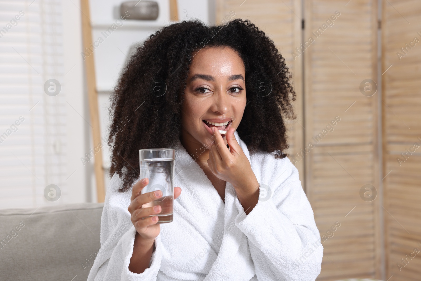 Beautiful Brazilian woman with glass of water taking collagen pill indoors Photo of Beautiful Brazilian woman with glass of water taking collagen pill indoors