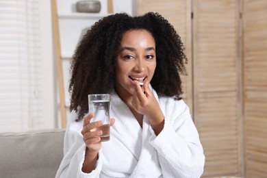 Photo of Beautiful Brazilian woman with glass of water taking collagen pill indoors
