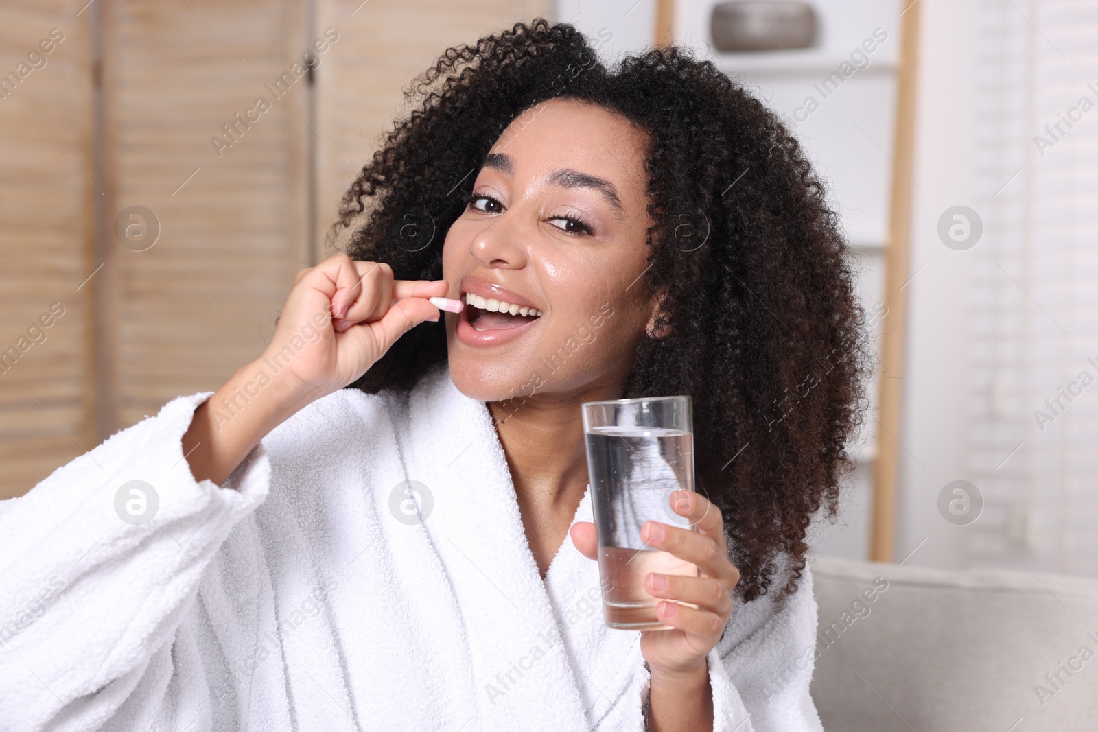 Beautiful Brazilian woman with glass of water taking collagen pill indoors Photo of Beautiful Brazilian woman with glass of water taking collagen pill indoors