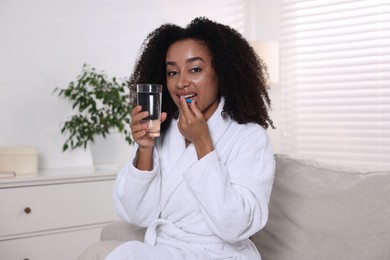 Photo of Beautiful Brazilian woman with glass of water and collagen pill indoors