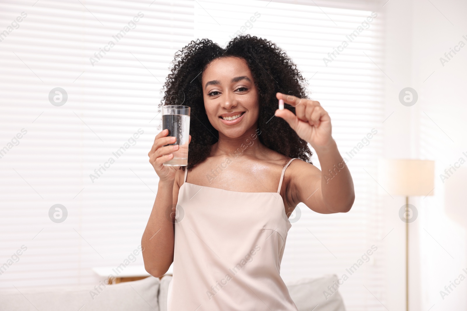 Beautiful Brazilian woman with glass of water and collagen pill indoors Photo of Beautiful Brazilian woman with glass of water and collagen pill indoors