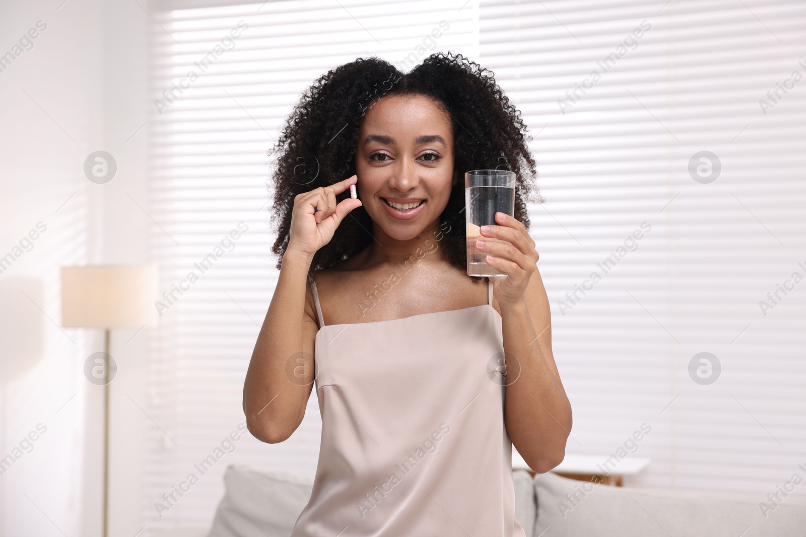 Beautiful Brazilian woman with glass of water and collagen pill indoors Photo of Beautiful Brazilian woman with glass of water and collagen pill indoors