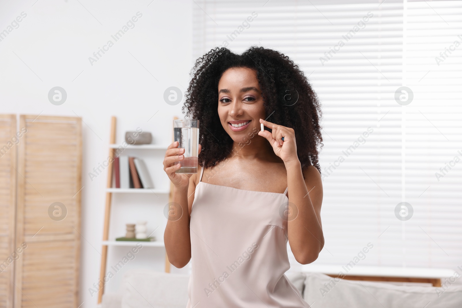 Beautiful Brazilian woman with glass of water and collagen pill indoors Photo of Beautiful Brazilian woman with glass of water and collagen pill indoors