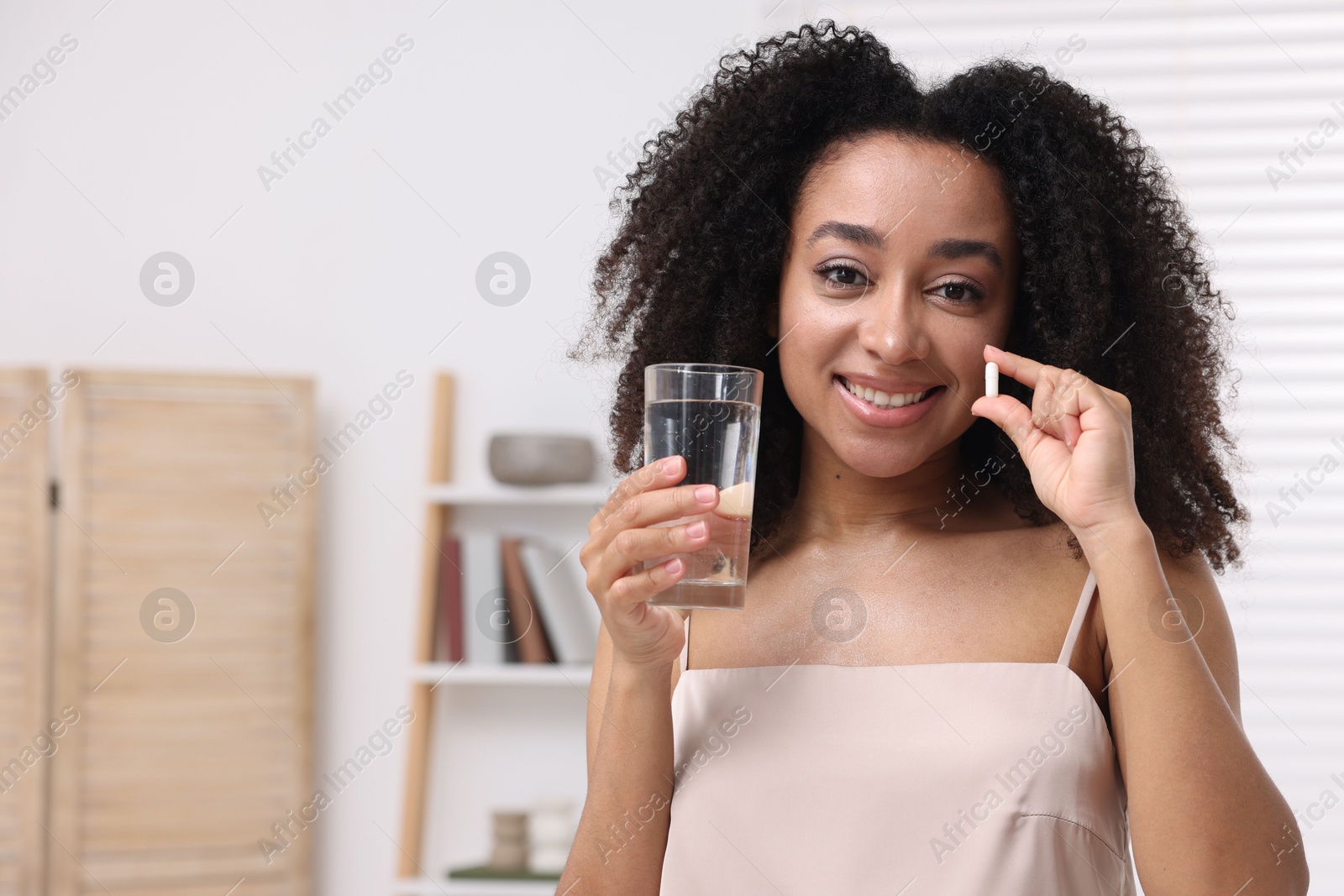 Beautiful Brazilian woman with glass of water and collagen pill indoors. Space for text Photo of Beautiful Brazilian woman with glass of water and collagen pill indoors. Space for text