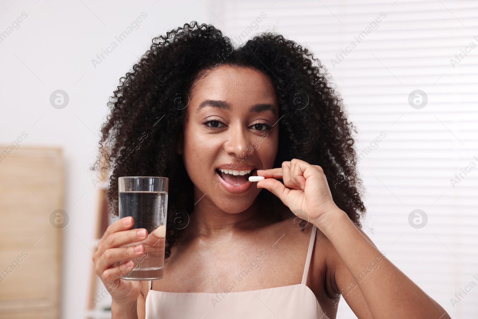 Beautiful Brazilian woman with glass of water taking collagen pill indoors Photo of Beautiful Brazilian woman with glass of water taking collagen pill indoors