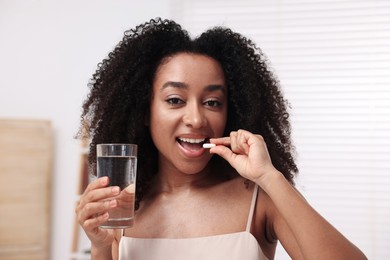 Photo of Beautiful Brazilian woman with glass of water taking collagen pill indoors
