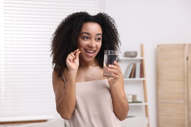 Photo of Beautiful Brazilian woman with glass of water and collagen pill indoors