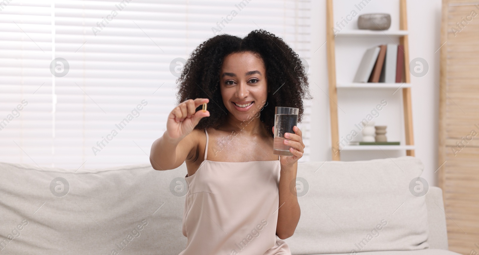Beautiful Brazilian woman with glass of water and collagen pill indoors Photo of Beautiful Brazilian woman with glass of water and collagen pill indoors