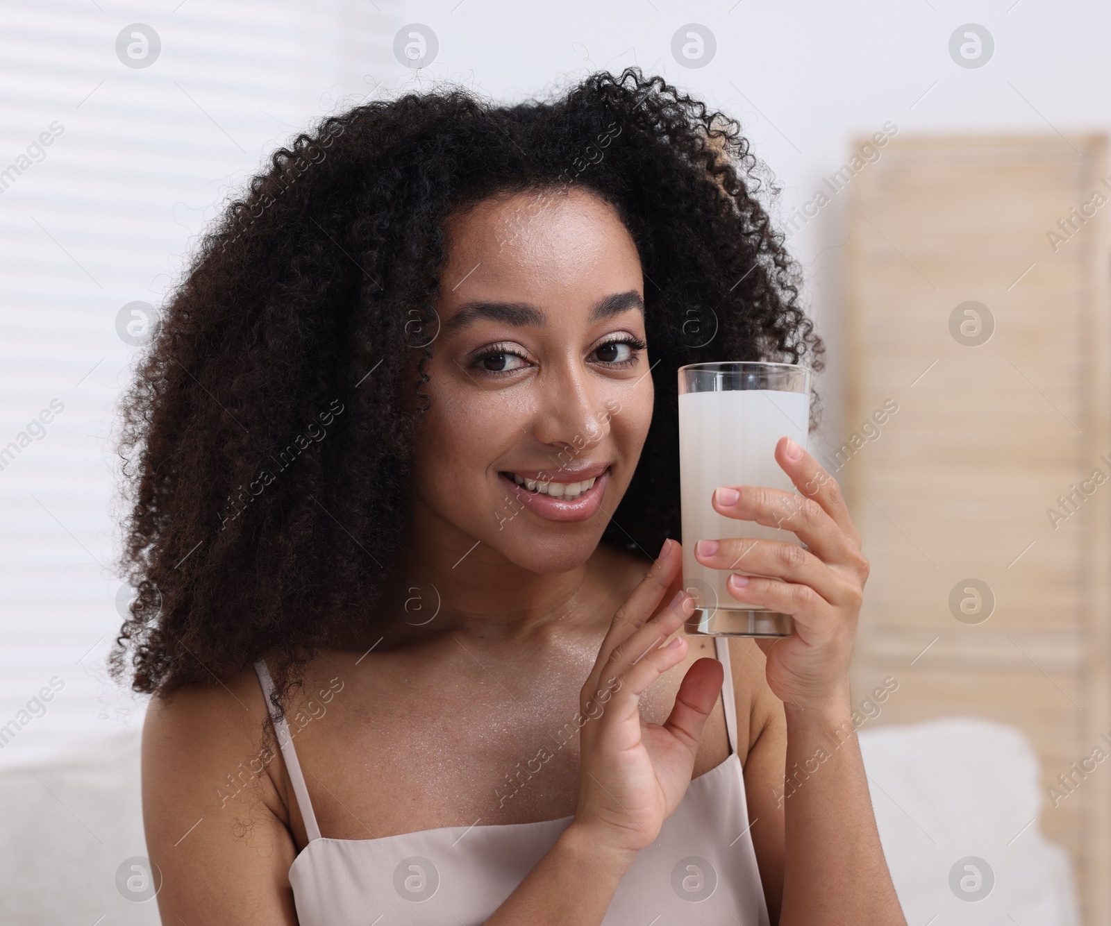 Beautiful Brazilian woman with glass of collagen water indoors Photo of Beautiful Brazilian woman with glass of collagen water indoors