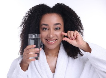 Photo of Beautiful Brazilian woman with glass of water and collagen pill on white background