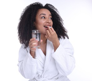 Photo of Beautiful Brazilian woman with glass of water taking collagen pill on white background
