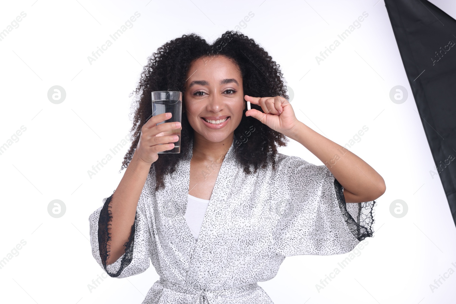 Beautiful Brazilian woman with glass of water and collagen pill on white background Photo of Beautiful Brazilian woman with glass of water and collagen pill on white background