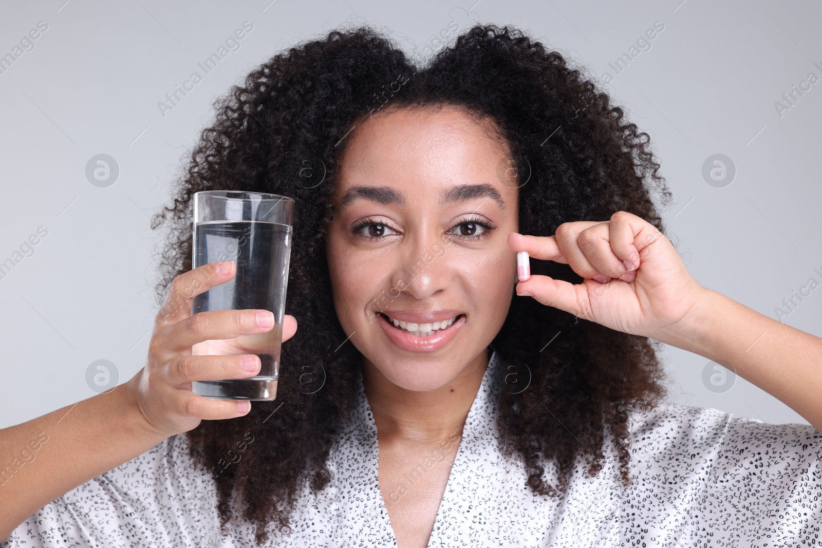 Beautiful Brazilian woman with glass of water and collagen pill on gray background Photo of Beautiful Brazilian woman with glass of water and collagen pill on gray background