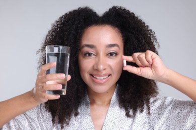 Photo of Beautiful Brazilian woman with glass of water and collagen pill on gray background