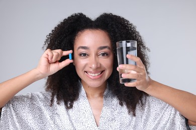Photo of Beautiful Brazilian woman with glass of water and collagen pill on gray background