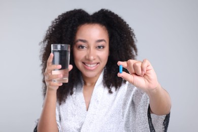 Photo of Beautiful Brazilian woman with glass of water and collagen pill on gray background, selective focus