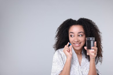 Photo of Beautiful Brazilian woman with glass of water and collagen pill on gray background. Space for text
