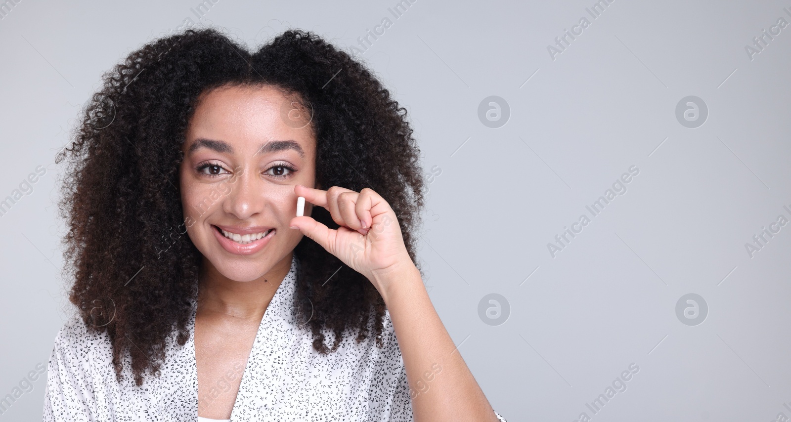 Beautiful Brazilian woman with collagen pill on gray background. Space for text Photo of Beautiful Brazilian woman with collagen pill on gray background. Space for text