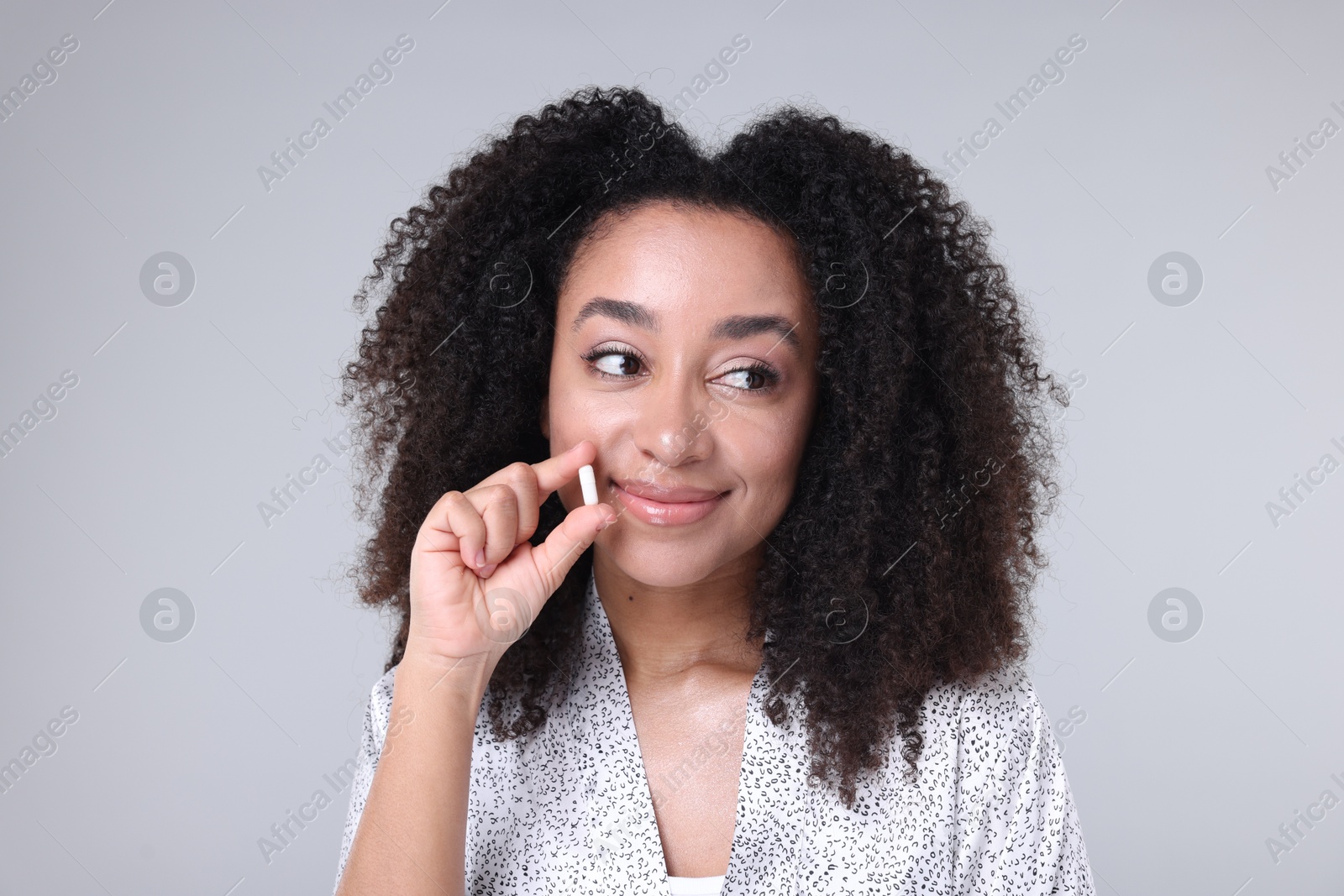 Beautiful Brazilian woman with collagen pill on gray background Photo of Beautiful Brazilian woman with collagen pill on gray background