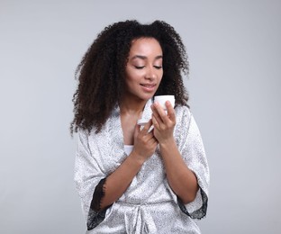 Photo of Beautiful Brazilian woman with jar of collagen cream on gray background