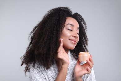 Photo of Beautiful Brazilian woman with jar of collagen cream on gray background