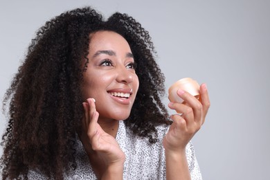 Photo of Beautiful Brazilian woman with jar of collagen cream on gray background
