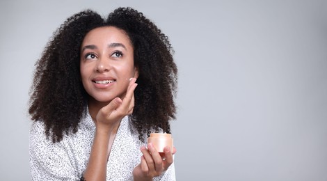 Photo of Beautiful Brazilian woman with jar of collagen cream on gray background. Space for text