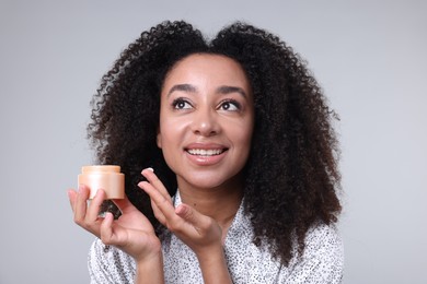 Photo of Beautiful Brazilian woman with jar of collagen cream on gray background