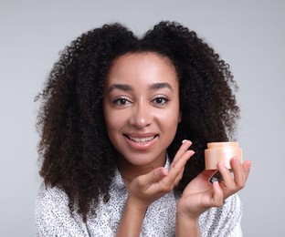 Photo of Beautiful Brazilian woman with jar of collagen cream on gray background