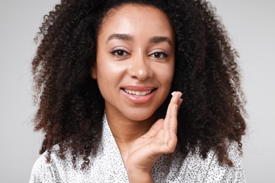 Photo of Beautiful Brazilian woman with collagen cream on gray background, closeup