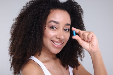 Photo of Beautiful Brazilian woman with collagen pill on gray background, closeup