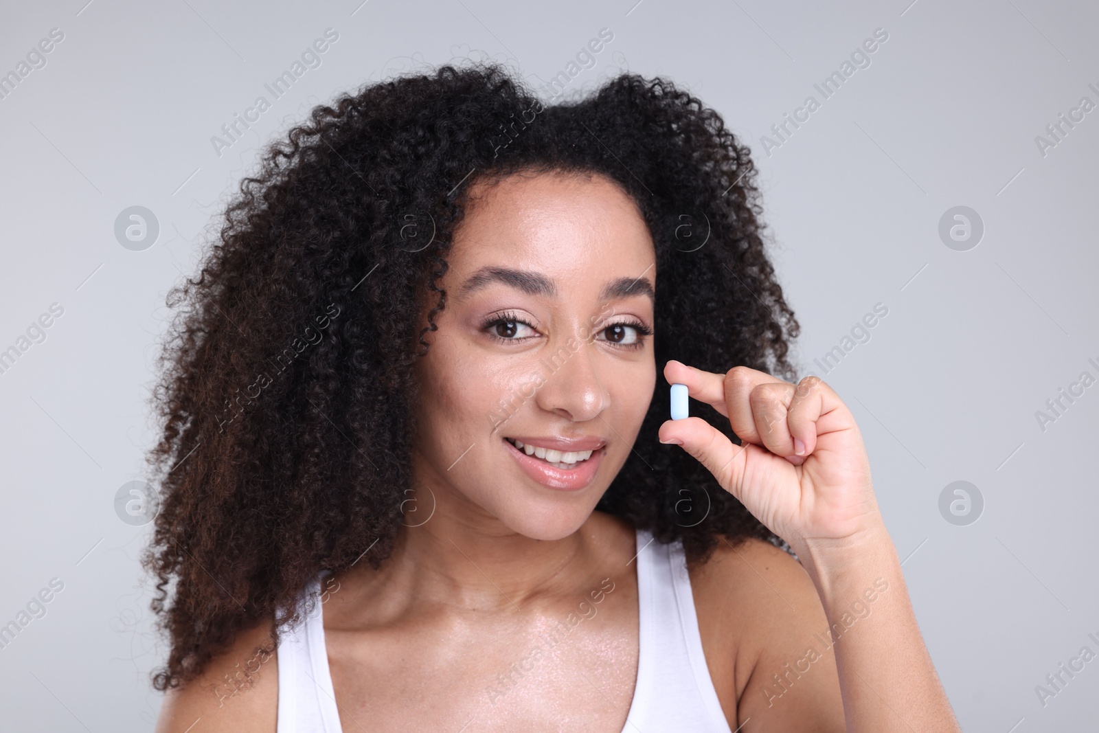 Beautiful Brazilian woman with collagen pill on gray background Photo of Beautiful Brazilian woman with collagen pill on gray background