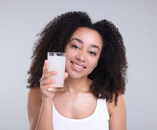 Photo of Beautiful Brazilian woman with glass of collagen water on gray background