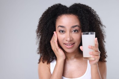 Photo of Beautiful Brazilian woman with glass of collagen water on gray background
