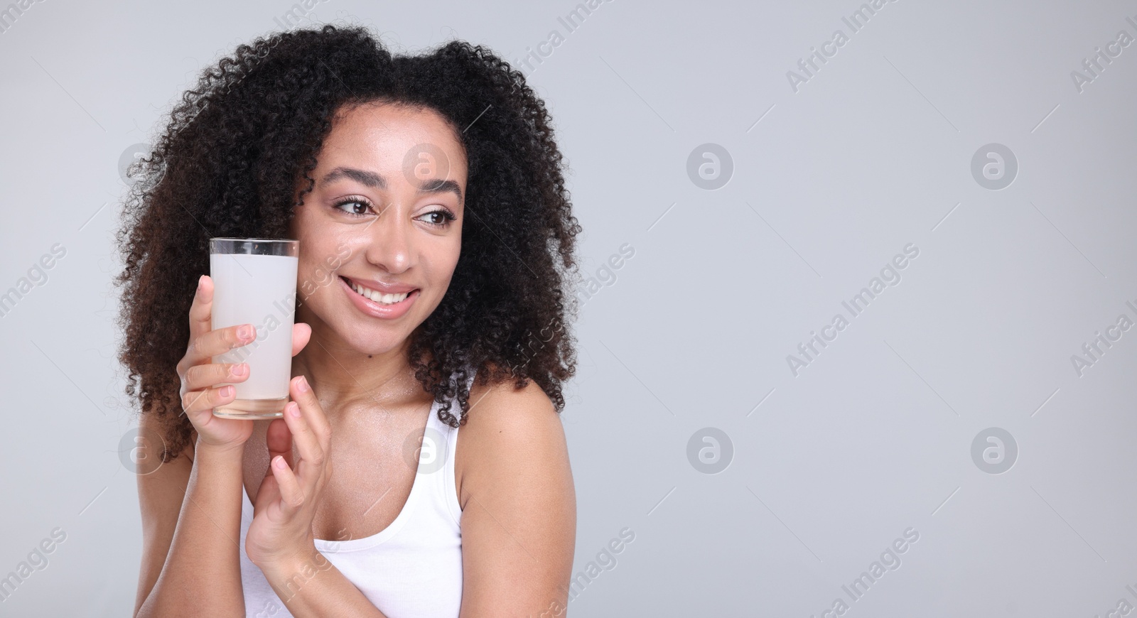 Beautiful Brazilian woman with glass of collagen water on gray background. Space for text Photo of Beautiful Brazilian woman with glass of collagen water on gray background. Space for text