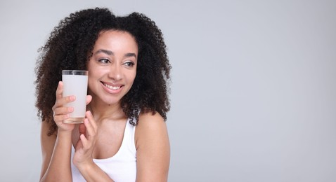 Photo of Beautiful Brazilian woman with glass of collagen water on gray background. Space for text