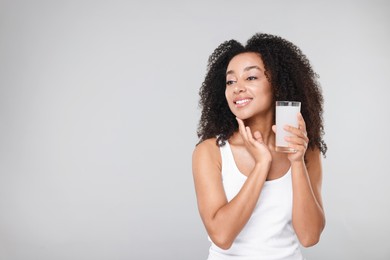Photo of Beautiful Brazilian woman with glass of collagen water on gray background. Space for text